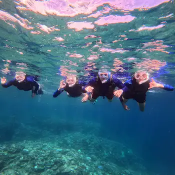 Four snorkelers underwater above a coral reef during a small-group Ishigaki shore excursion